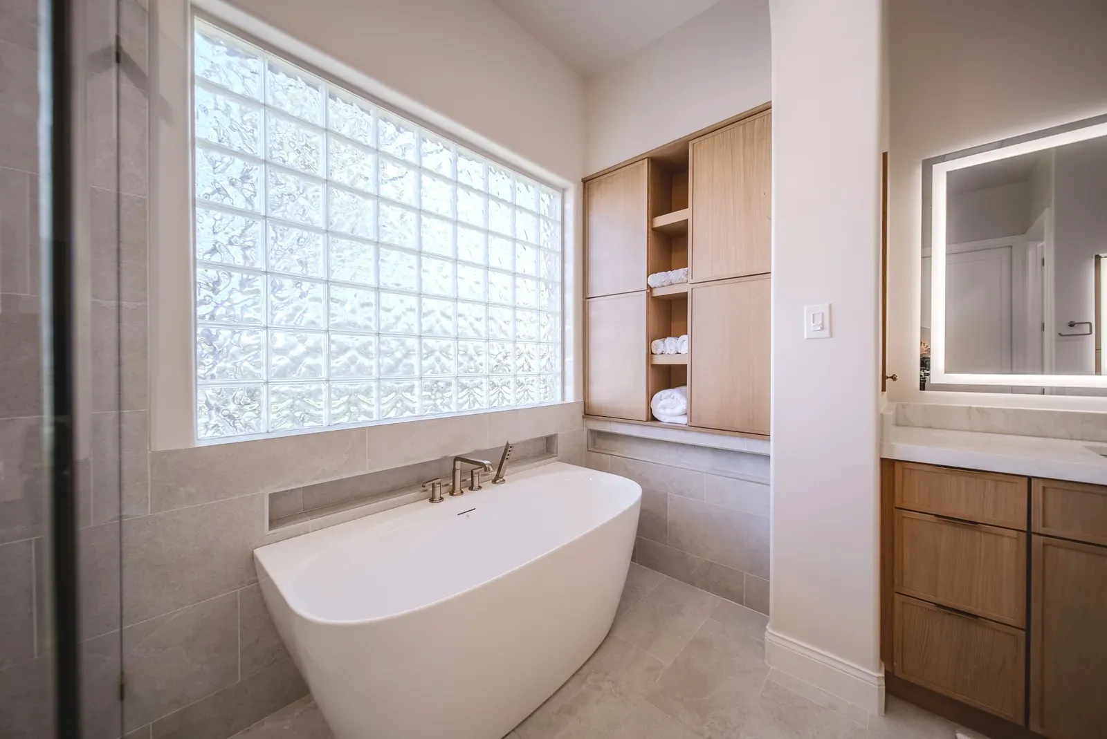 Freestanding soaking tub under a glass-block window in a remodeled Lake Travis primary bathroom