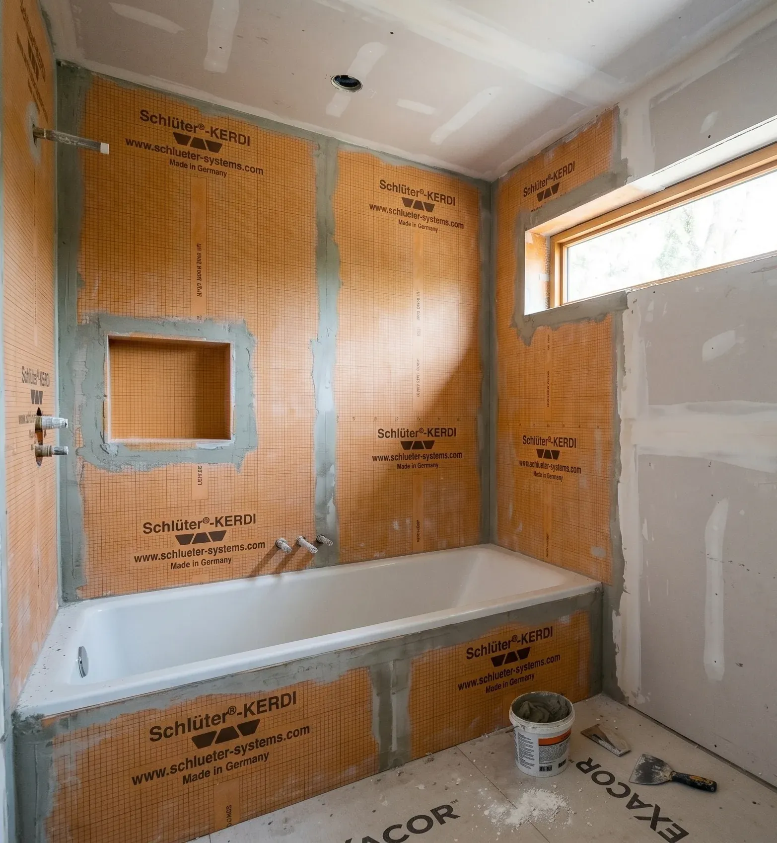 Bathroom mid-rebuild: the tub alcove sealed in orange waterproofing membrane below the clerestory window