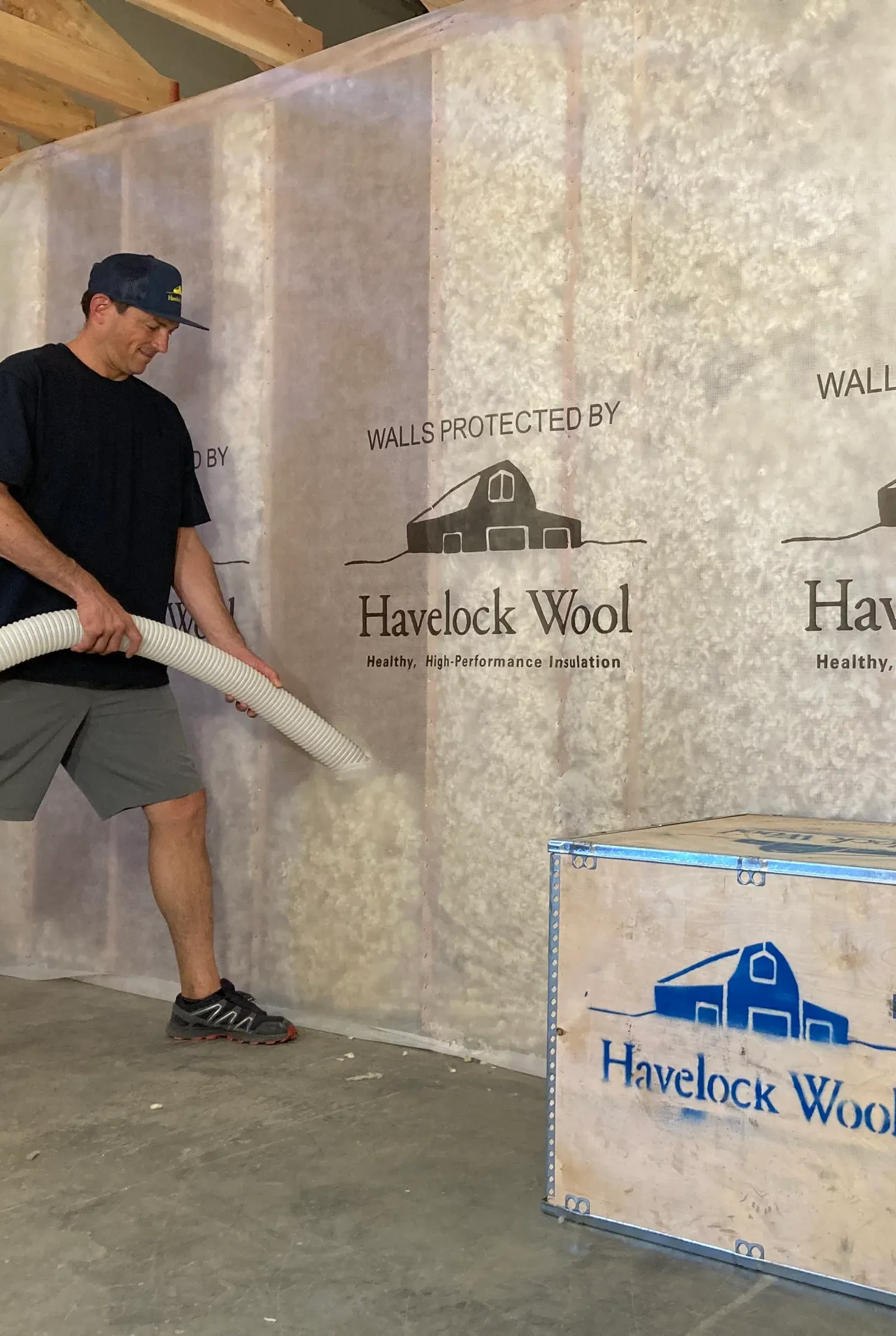 Installer blowing loose-fill wool insulation into netted wall cavities