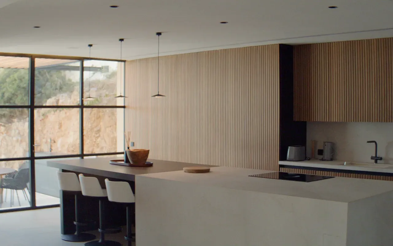 Open kitchen with slatted oak walls, pendant lights, a stone island and floor-to-ceiling windows onto a rock garden